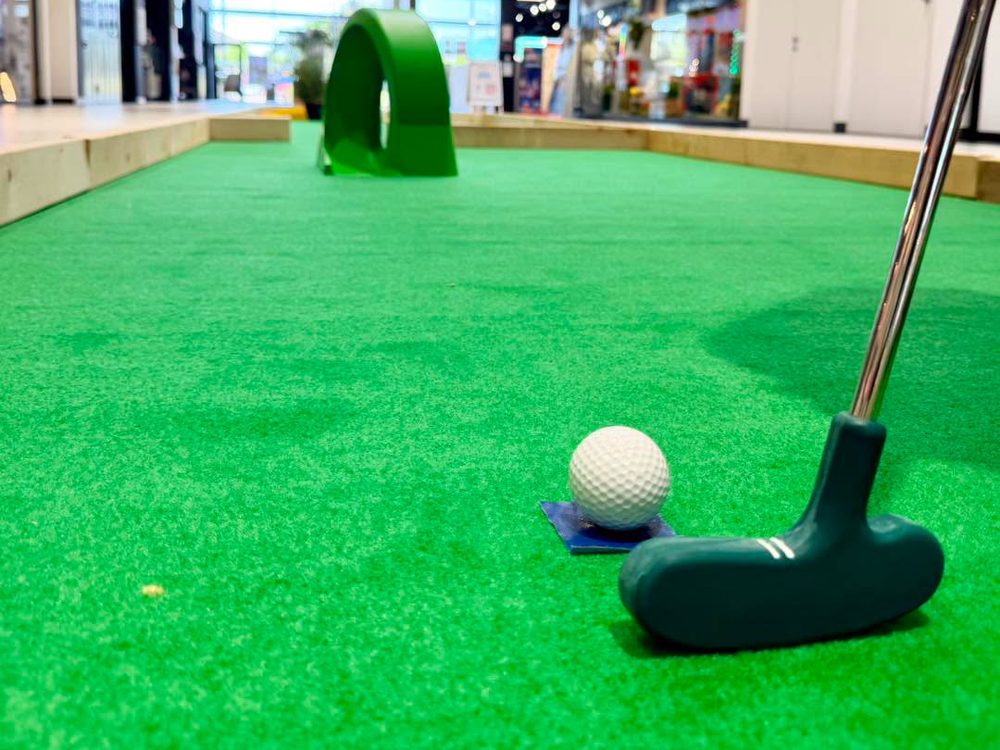 Balle et club de mini-golf sur la moquette verte d'une piste, dans une galerie marchande