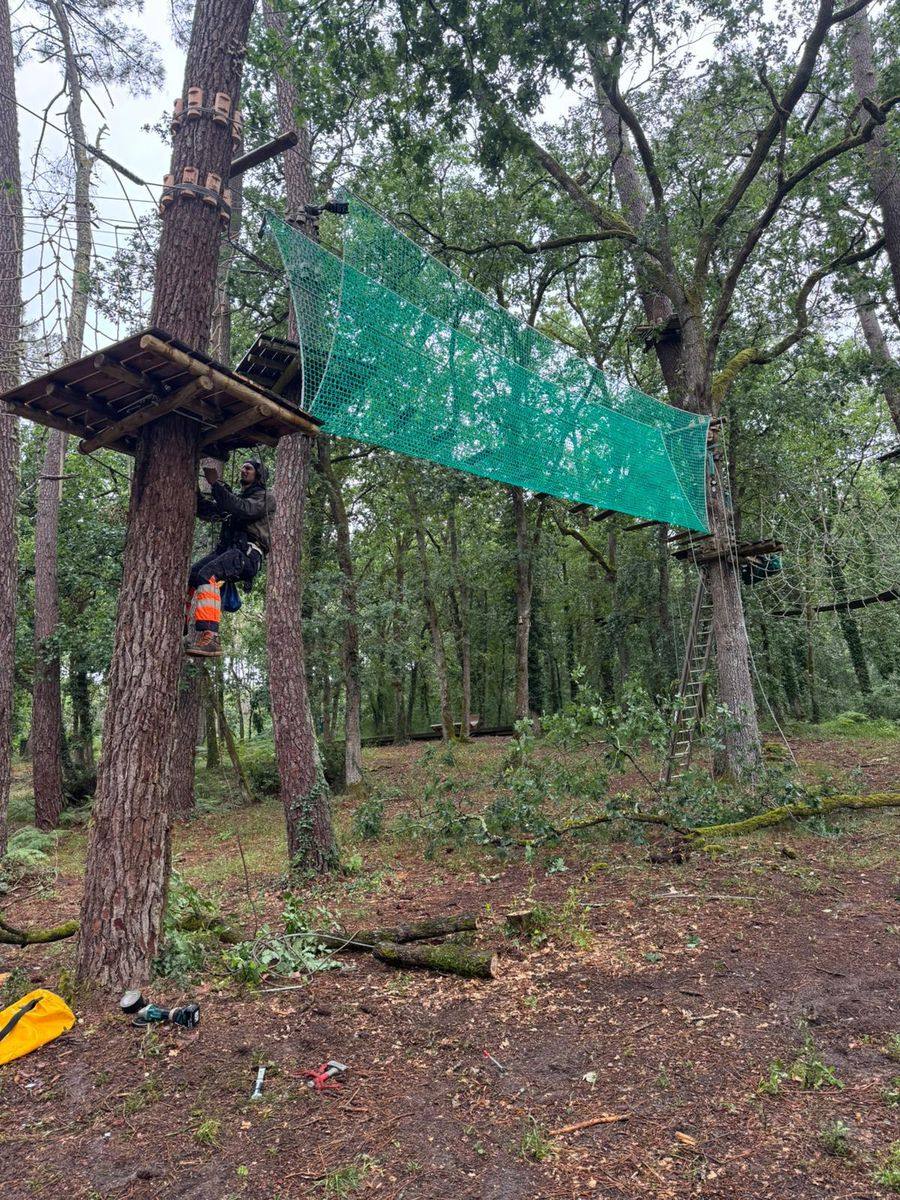 Chantier de construction accrobranche : pose d'une zone de filets entre deux plateformes dans un parc aventure
