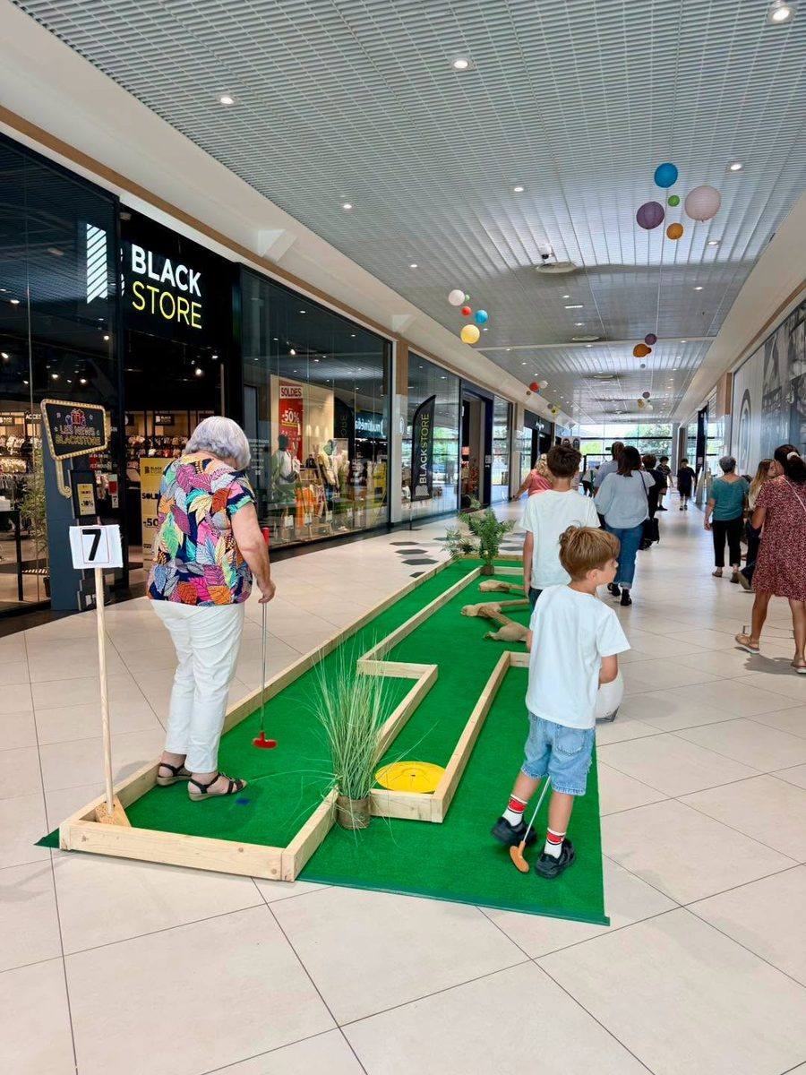 Une grand-mère et des enfants jouent au mini-golf mobile dans la galerie d'un centre commercial