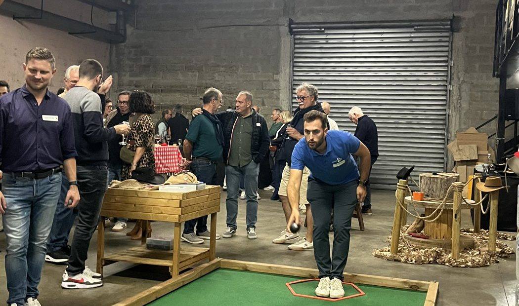 Joueur lançant une boule de pétanque indoor sur une piste en moquette verte, pendant une soirée d'entreprise