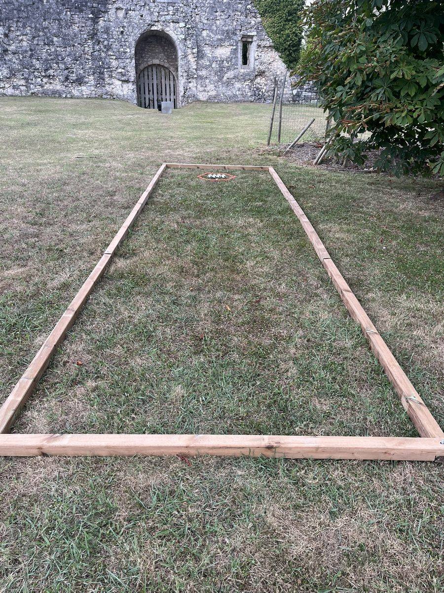 Terrain de pétanque outdoor délimité par un cadre en bois, installé sur la pelouse d'un château